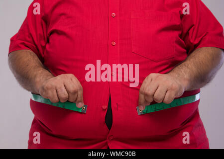 Close up uomo obesi misurando il suo stomaco in sovrappeso con un nastro di misurazione Foto Stock