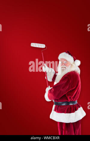 Babbo Natale dipinge un muro contro lo sfondo rosso Foto Stock