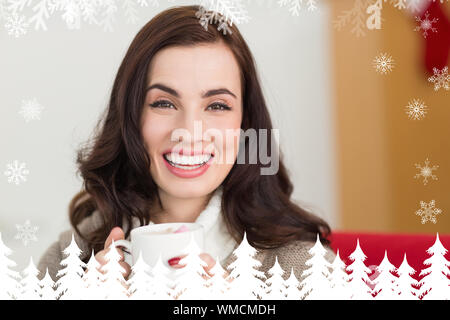 Sorridente brunette godendo di una cioccolata calda con marshmallow contro la foresta di abeti e i fiocchi di neve Foto Stock