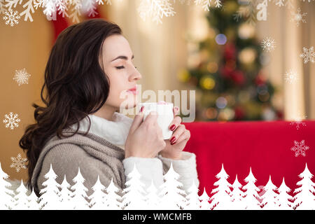 Brunette godendo di una cioccolata calda a Natale contro la foresta di abeti e i fiocchi di neve Foto Stock