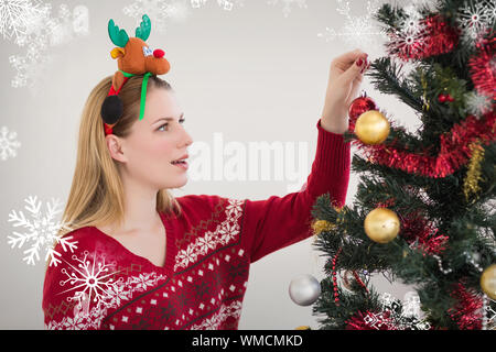 Donna Appendere le decorazioni di Natale su albero contro i fiocchi di neve Foto Stock