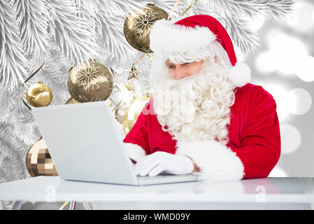 Santa utilizzando laptop contro le decorazioni di Natale appeso dal ramo Foto Stock