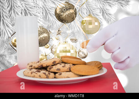 Mano di santa tenendo cookie contro le decorazioni di Natale appeso dal ramo Foto Stock