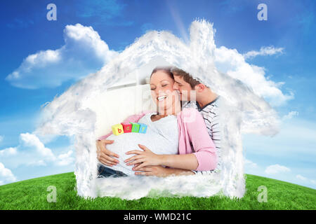 Ritratto di una allegra donna incinta con cubetti di bambino sul suo ventre e di suo marito bacia contro la collina verde sotto il cielo blu Foto Stock