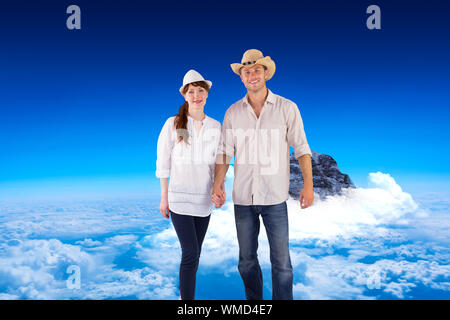 Coppia sorridente entrambi indossare cappelli contro il picco di montagna attraverso le nuvole Foto Stock