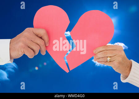 Giovane in possesso di una carta rotto cuore luminoso contro il cielo blu con nuvole Foto Stock