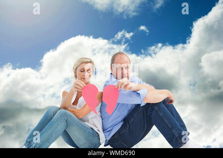 Triste Coppia matura tenendo un cuore spezzato contro il cielo blu con nuvole Foto Stock