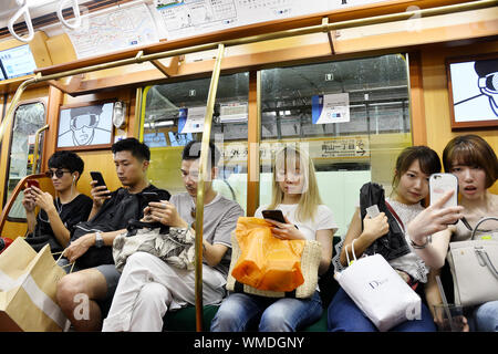 Passeggeri che utilizzano i loro smartphone mentre viaggiano su un treno della metropolitana di Tokyo in Giappone Foto Stock