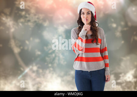 Festive brunette in santa hat mantenendo un segreto contro sfocata sullo sfondo di Natale Foto Stock