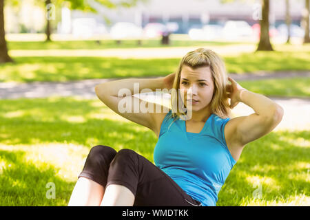 Montare la bionda facendo sit ups nel parco in una giornata di sole Foto Stock