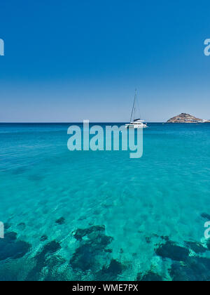 Moderno yacht a vela in acque turchesi dell'oceano in condizioni di luce solare intensa contro il cielo blu chiaro Foto Stock