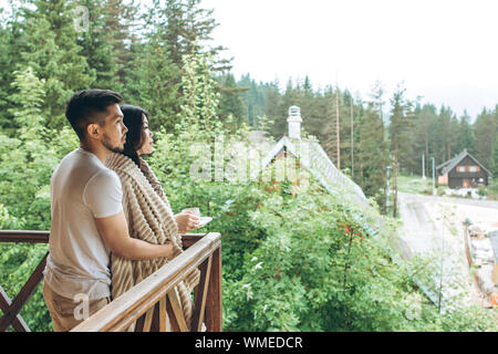 Un uomo abbraccia una donna sul balcone e guardano in lontananza o sogno. Foto Stock