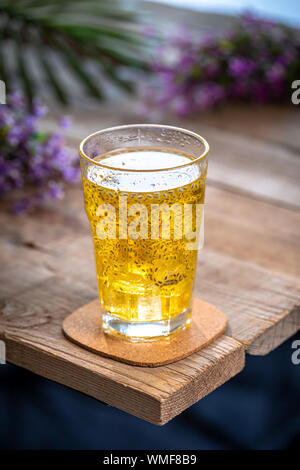 Un bicchiere di semi di chia dorati beve su un tavolo di legno con fiori viola sullo sfondo. Foto Stock