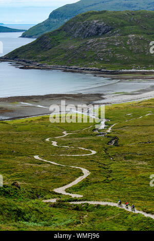 Tre i ciclisti di montagna corsa giù per un sentiero per Camasunary Beach sull'Isola di Skye sulla costa ovest della Scozia durante l'estate. Foto Stock