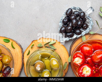 Mix di olive in olio di oliva con erbe aromatiche, rosso peperoni ripieni di formaggio su sfondo grigio Foto Stock