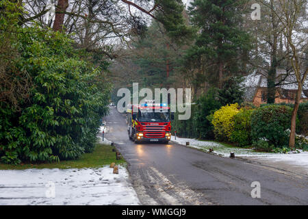 Un rosso Scania P270 motore fire con luci lampeggianti assiste ad una situazione di emergenza in un freddo mattino nevoso in inverno, Woking, Surrey, Inghilterra del sud-est Foto Stock