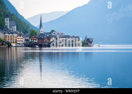 Vista di una montagna villaggio austriaco sulla riva di un lago alpino su uno sfondo di montagne i raggi del sole al tramonto. Hallstatt. Hallstat Foto Stock