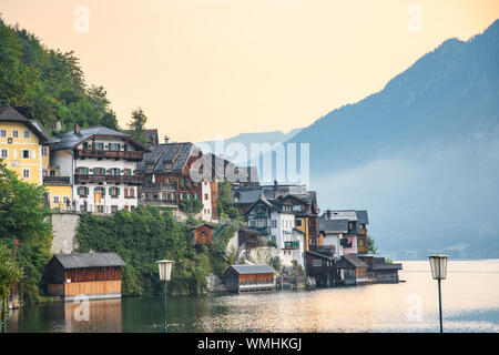 Vista di una montagna villaggio austriaco sulla riva di un lago alpino su uno sfondo di montagne i raggi del sole al tramonto. Hallstatt. Hallstat Foto Stock