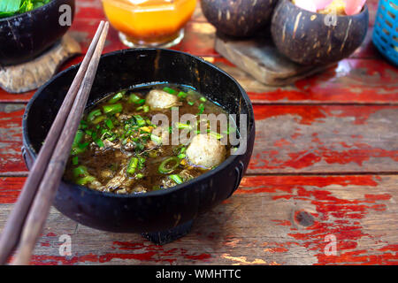 Thai noodles nella ciotola di legno guscio di noce di cocco e bastoncini realizzati a mano su un tavolo di legno Foto Stock