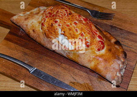 Calzone di pizza su una superficie di legno, con coltello e forchetta Foto Stock