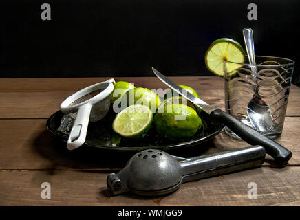 I limoni tagliati per la limonata su una tavola di legno in uno sfondo scuro con una spremitore limone un bicchiere e un coltello Foto Stock