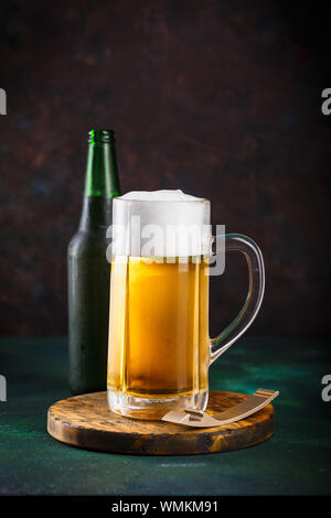 Tazza di vetro con la birra con la schiuma e gocce di acqua su un sfondo verde scuro