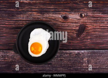 Uovo fritto in padella, su sfondo di legno. Vista dall'alto. Foto Stock