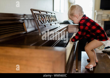 Baby boy nel pannolino sorge su banco suonare il pianoforte a casa Foto Stock