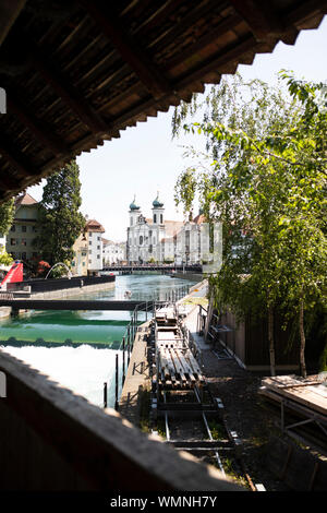 Il weir con la sua storica diga ad aghi sul ponte Spreuerbrücke sul fiume Reuss a Lucerna, in Svizzera, con la chiesa gesuita in lontananza. Foto Stock