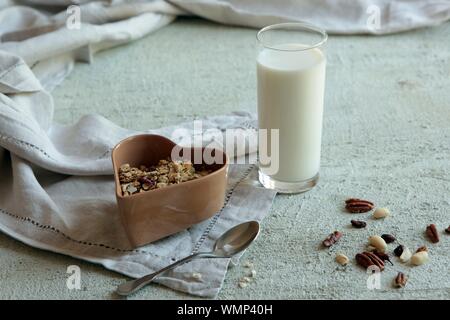 Ciotola di muesli fatti in casa con i dadi, frutti di bosco e frutta secca, un bicchiere di latte e miele. una sana prima colazione. Foto Stock