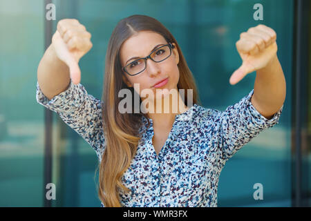 Sconvolto giovane donna di affari con il pollice verso il basso all'esterno. Foto Stock