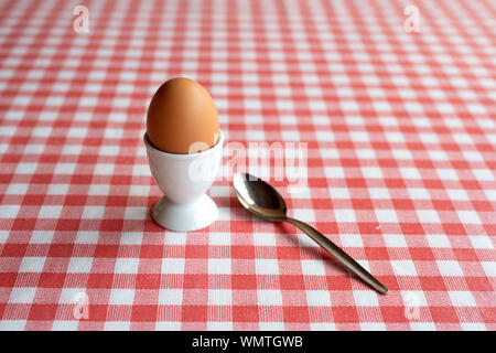 Singolo uovo bollito con cucchiaio pronto a mangiare su un tavolo Foto Stock