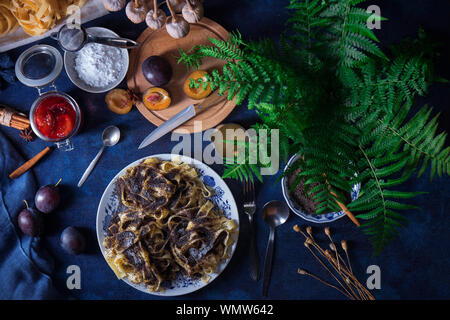 Pasta dolce dessert, tagliatelle con semi di papavero, prugna composta di prugne fresche, sfondo scuro, tavolo blu decorato con fiori freschi. Tutto secco popp Foto Stock