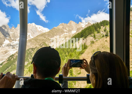 Un giovane da dietro a bordo di una cabina del Skyway Monte Bianco funivia con la donna a scattare foto con il suo smartphone, Courmayeur, Italia Foto Stock