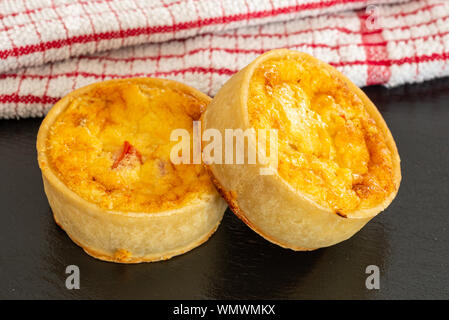 Due piccole quiche servita su un nero ardesia vassoio fresco di forno. Foto Stock