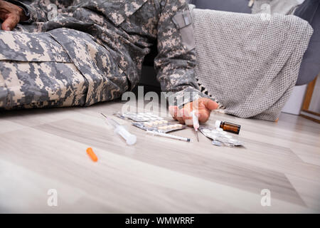 Siringa e la Confezione Blister di pillole caduti sul pavimento vicino a disabilita ufficiale dell'esercito a casa Foto Stock