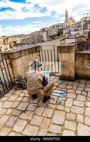 In Italia, Basilicata, provincia di Matera, Matera. Maggio 28, 2019. Un artista su un tetto di verniciatura di un acquerello di vista della città, dominata dalla cattedra Foto Stock