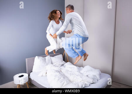 Felice amorevole Coppia Matura saltando su letto di casa Foto Stock