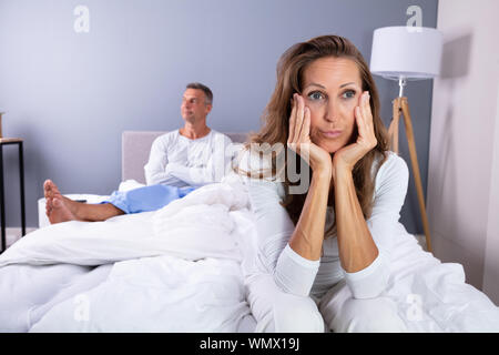 Infelice Coppia Matura seduta sul letto in camera da letto Foto Stock