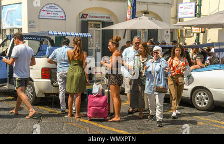 Isola di Capri - Agosto 2019: persone con bagagli al taxi nella porta sull'Isola di Capri dopo che arrivano su un traghetto. Foto Stock