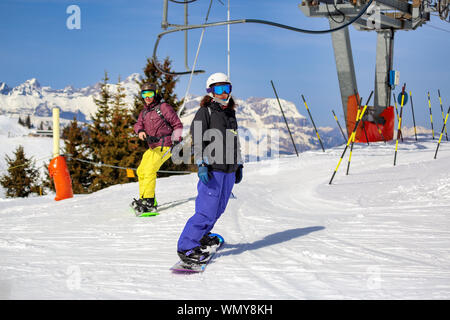 Due snowboarder che si riscaldano alla pista in una giornata di sole a Megeve della regione di Chamonix sulle Alpi francesi. Impianti di risalita e alberi sullo sfondo. Foto Stock