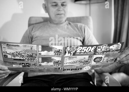 Parigi, Francia - 22 Maggio 2019: Senior uomo lettura ampia flyer pubblicità che presentano sul coperchio di più prodotti domestici offerti da esperti Oehler - 4k TV Imposta , macchine di lavaggio Foto Stock