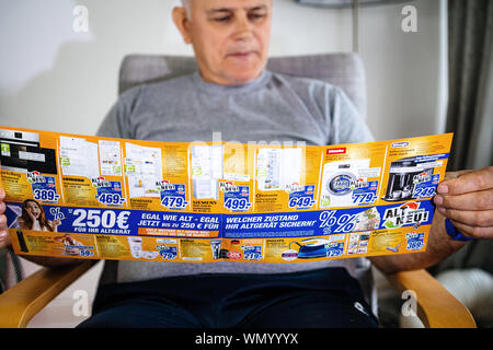 Parigi, Francia - 22 Maggio 2019: Senior man holding flyer pubblicità che presentano sul coperchio di più prodotti domestici offerti da esperti Oehler - macchine di lavaggio, expressos, frigoriferi, ferro da stiro, epilatori Foto Stock