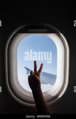 Silhouette di mano della ragazza facendo segno di pace dalla finestra di aeroplano Foto Stock