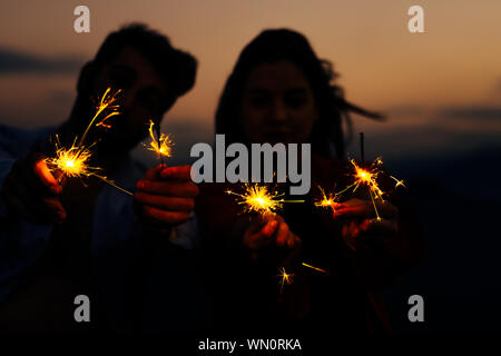 Botti di illuminazione masterizzare in maschio e femmina con le mani su notte scura sullo sfondo del tramonto Foto Stock