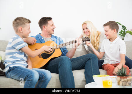 Felice famiglia caucasica sorridente, suonare la chitarra e cantare canzoni insieme a accogliente casa moderna Foto Stock