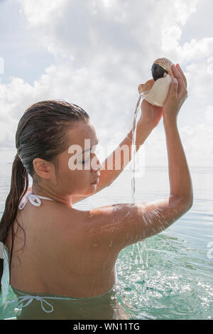 Donna in mare versando acqua fuori di nautilus conchiglia Foto Stock