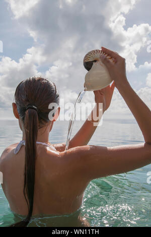 Donna in mare versando acqua fuori di nautilus conchiglia Foto Stock