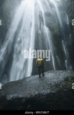 Uomo che indossa un impermeabile giallo da cascata Seljalandsfoss in Islanda Foto Stock