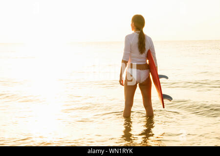 Donna che mantiene le tavole da surf in mare al tramonto Foto Stock